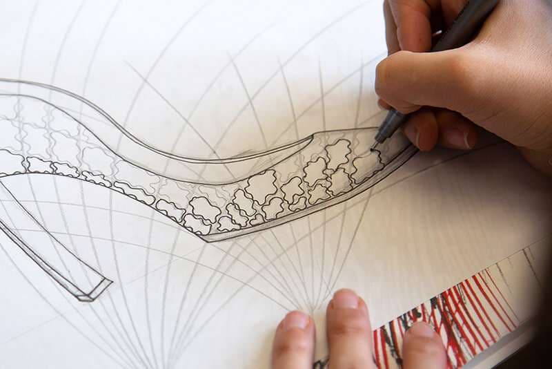 Mano che disegna una scarpa con tacco decorato, dettaglio del corso di design