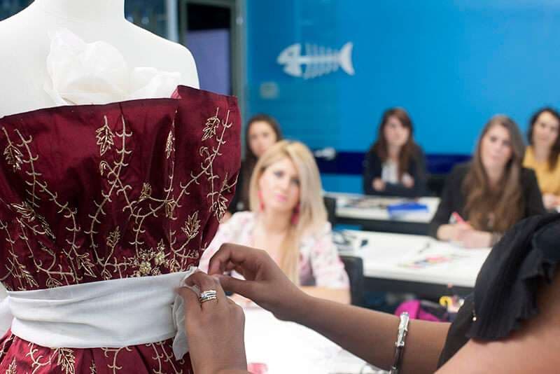 Manichino con abito ricamato in oro e allieva che lavora sulla stoffa
