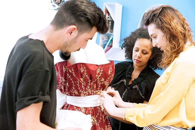 Docente Eden Embafrash segue due allievi al lavoro su un abito ricamato