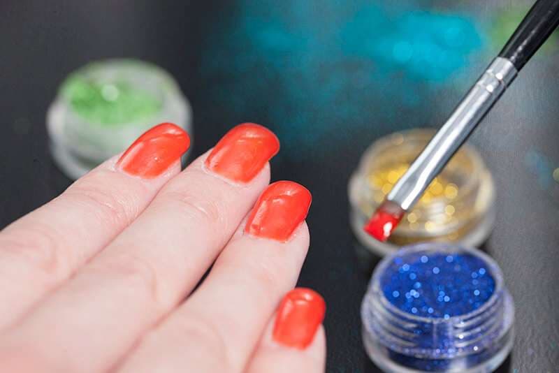 Dettaglio unghie rosse con pennello e prodotti professionali
