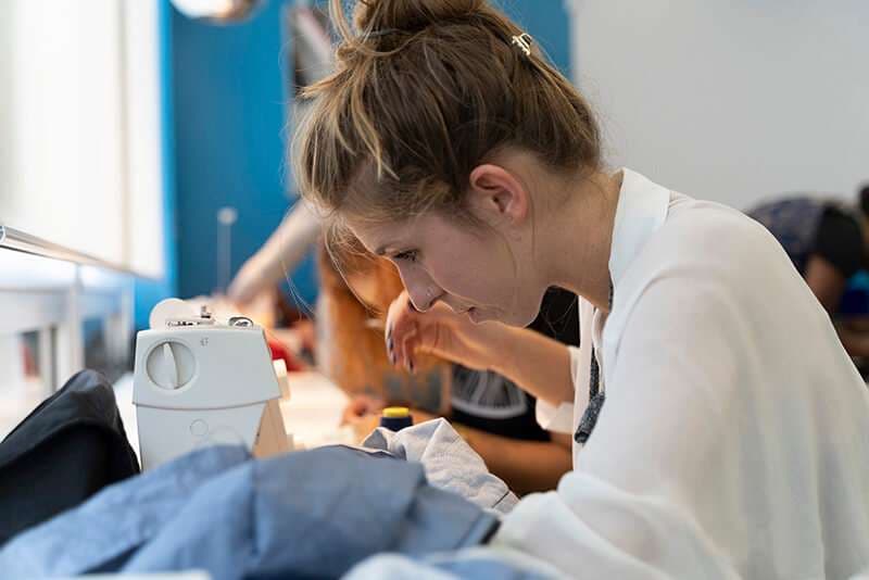 Allieva AreaDomani concentrata al lavoro sulla macchina da cucire durante il corso Sartoria