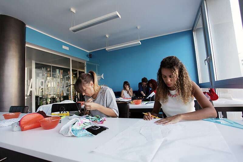 Aula AreaDomani Sartoria con vetrata luminosa, tavolo taglio e biblioteca di moda, Via Varese 1 Genova